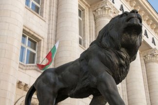Na pierwszym planie widać pomnik lwa, zaś na drugim flagę Bułgarii 