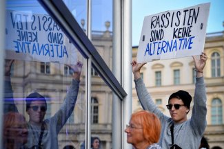 Pierwszy plan po prawej stronie młody demonstrant z hasłem: Rassisten sind keine alternative. Po lewej stronie widać jego odbicie w lustrze. 