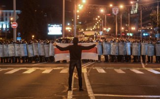 Protesty na Białorusi. Mężczyzna z flagą stoi naprzeciwko sił porządkowych