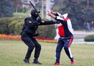 Zdjęcie przedstawia funkcjonariusza, który bije jednego z protestującyh
