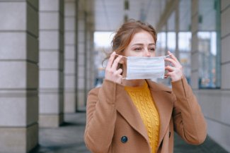 The photo shows a woman putting on a protective mask.